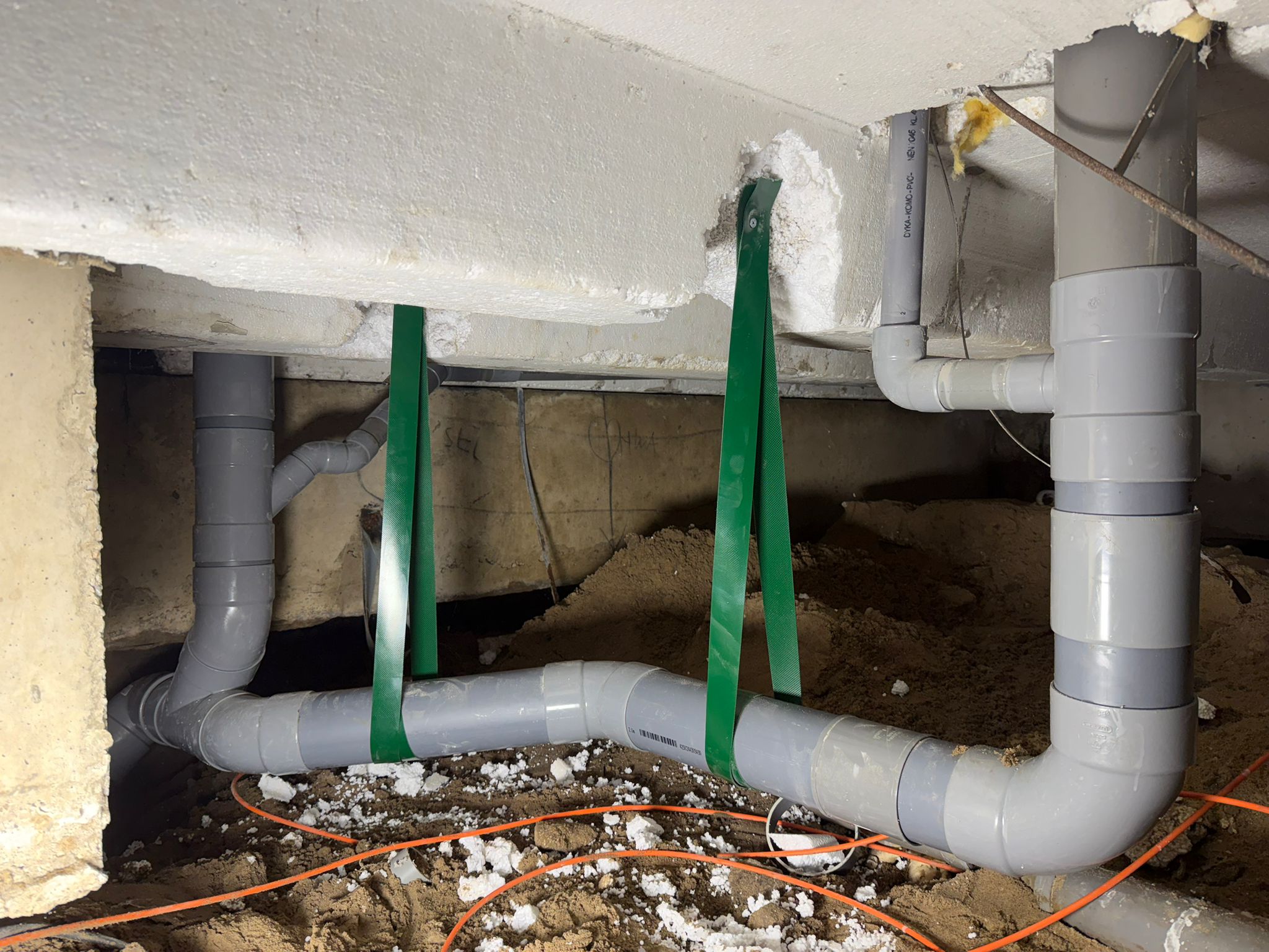 Nieuwe grijze PVC-afvoer in de kruipruimte, opgehangen met groene banden