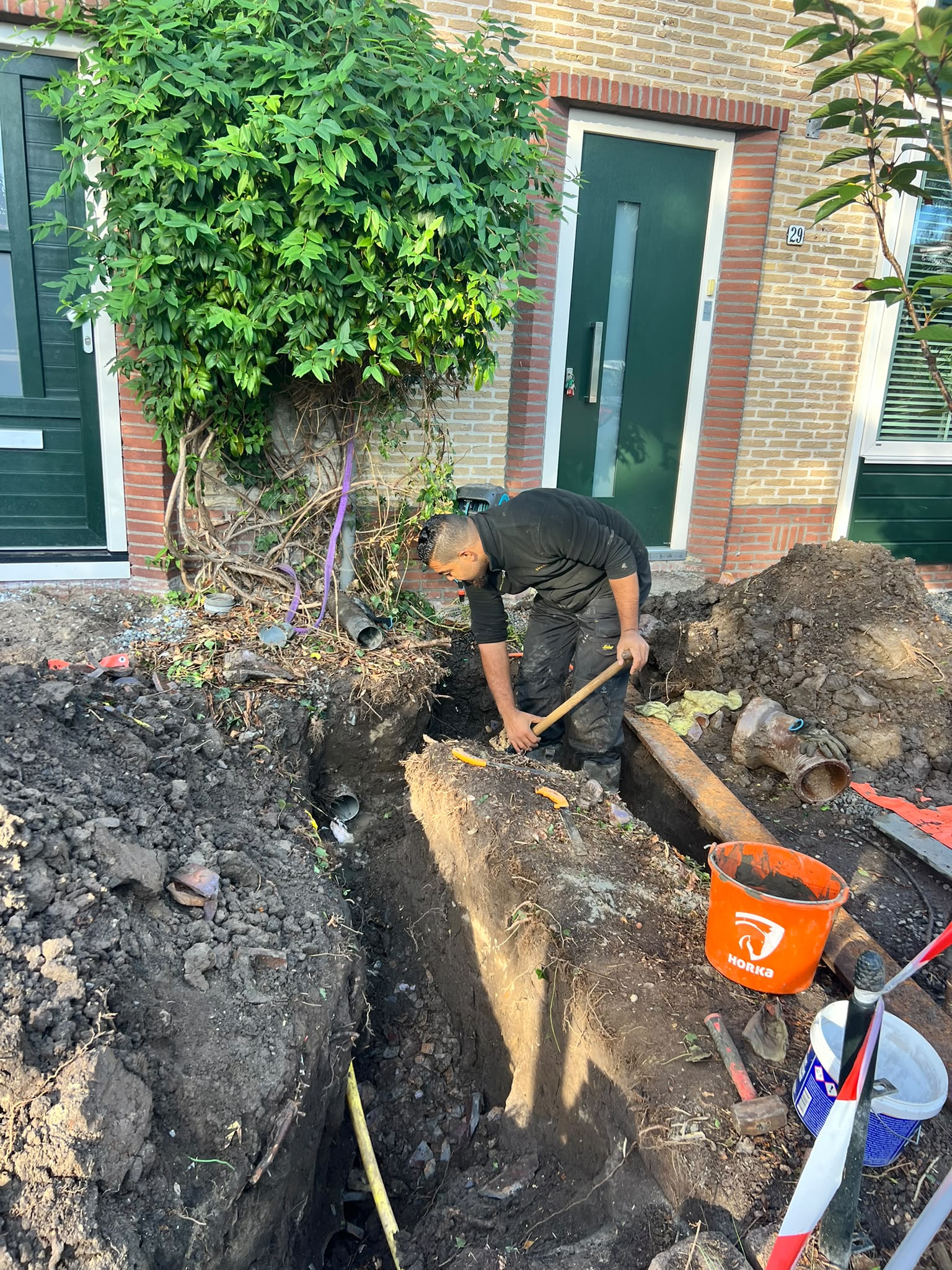Monteur graaft een diepe sleuf door de voortuin om de rioolleiding bloot te leggen