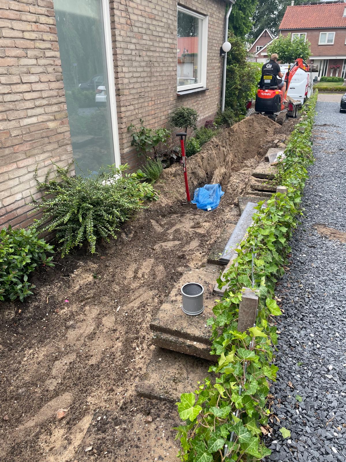 Lange open sleuf door de voortuin, langs de gevel van de woning