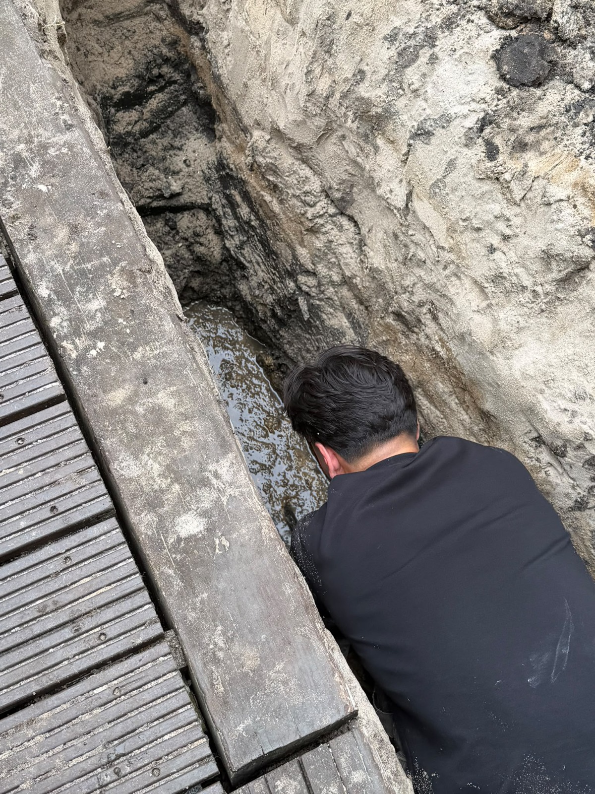 Monteur buigt in een diepe sleuf over de blootgelegde rioolleiding